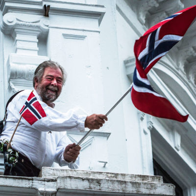 Jovial Man Hoisting the National Flag at the Balcony of his own House, in the City of Bergen